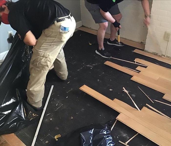 two male SERVPRO employees removing pieces of floor boards in dining room
